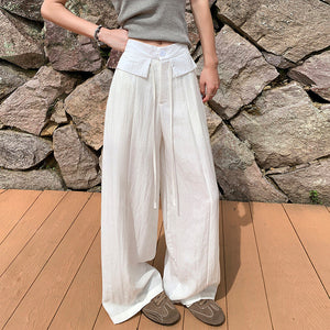 White wide leg summer pants with self tie belt against a stone wall