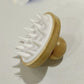 White bamboo silicone scalp massage brush resting on its rounded wooden knob handle