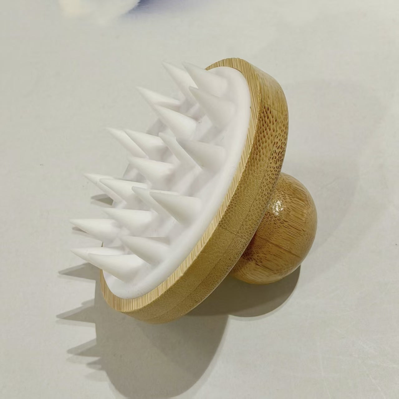 White bamboo silicone scalp massage brush resting on its rounded wooden knob handle