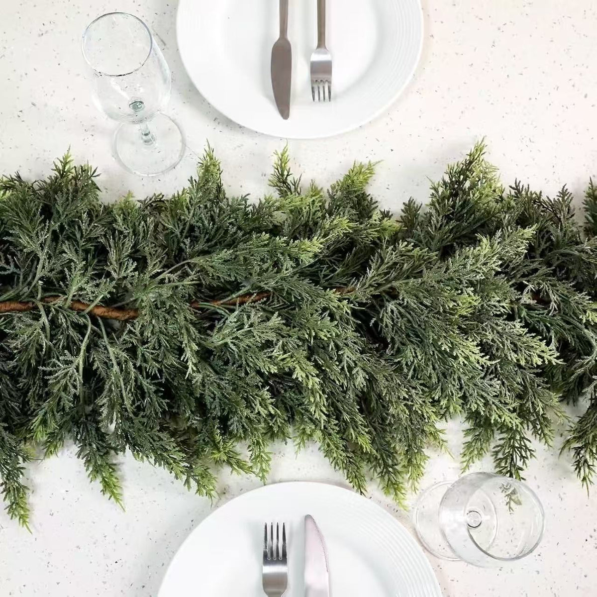 Top down view of the cedar garland as a table runner between two white place settings and wine glasses