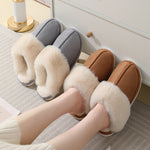 Gray and brown plush cuff slip-on mule slippers on a striped rug beside a pair of feet