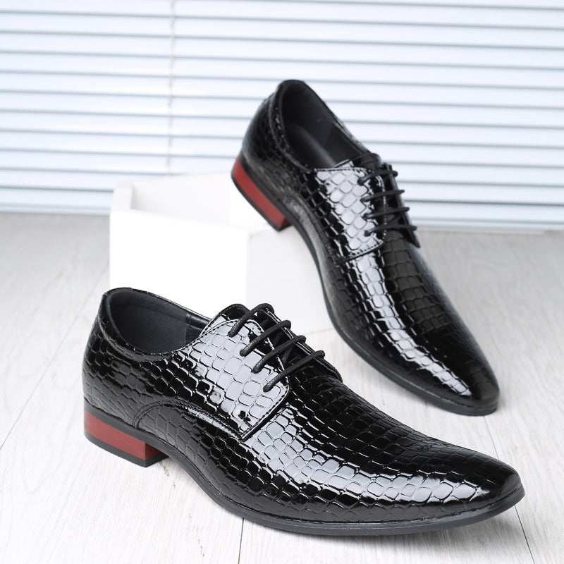Pair of black croc embossed derby shoes with pointed toes and red-brown heels on a white block