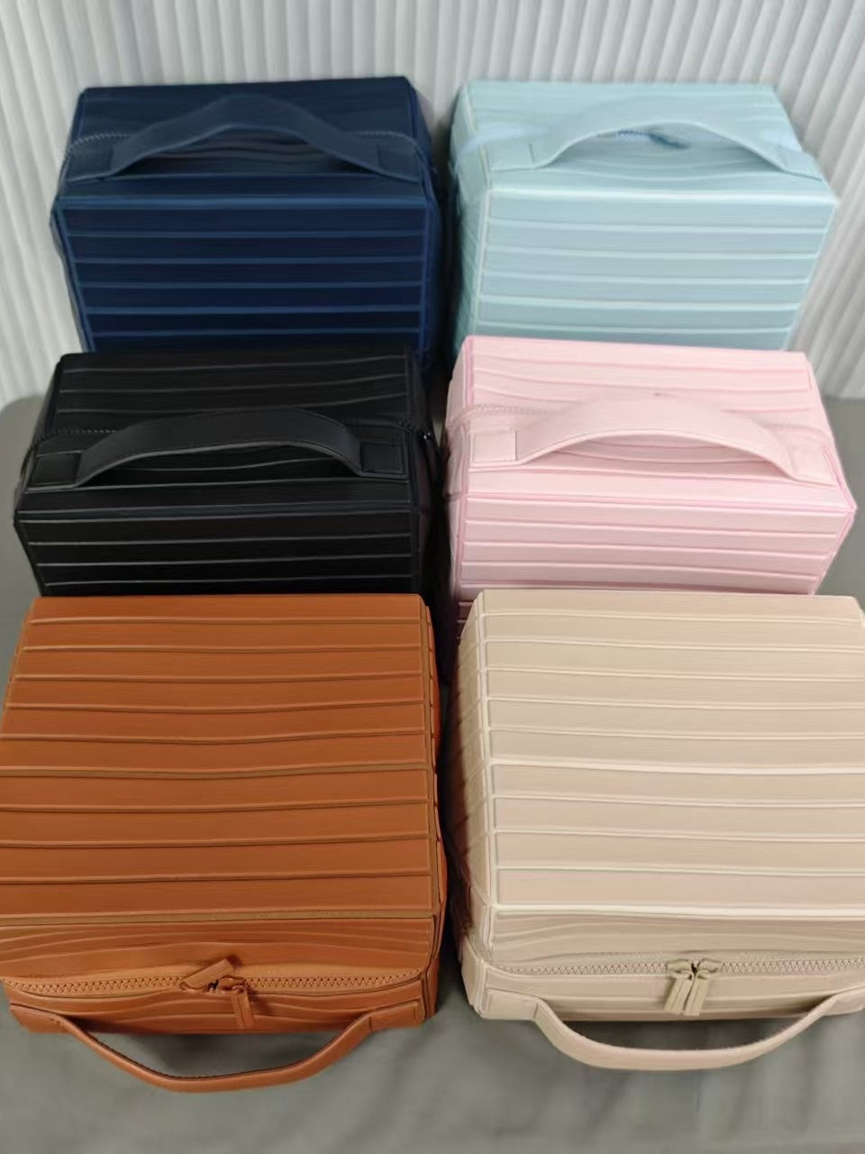 Six ribbed stripe makeup organizer cases stacked in navy, light blue, black, pink, brown and apricot