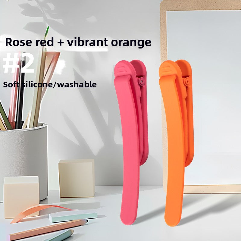 Two piece set of silicone bookmark clips in rose red and vibrant orange on a desk