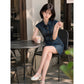 Woman seated in short blue denim shirt dress with fitted waist and cap sleeves