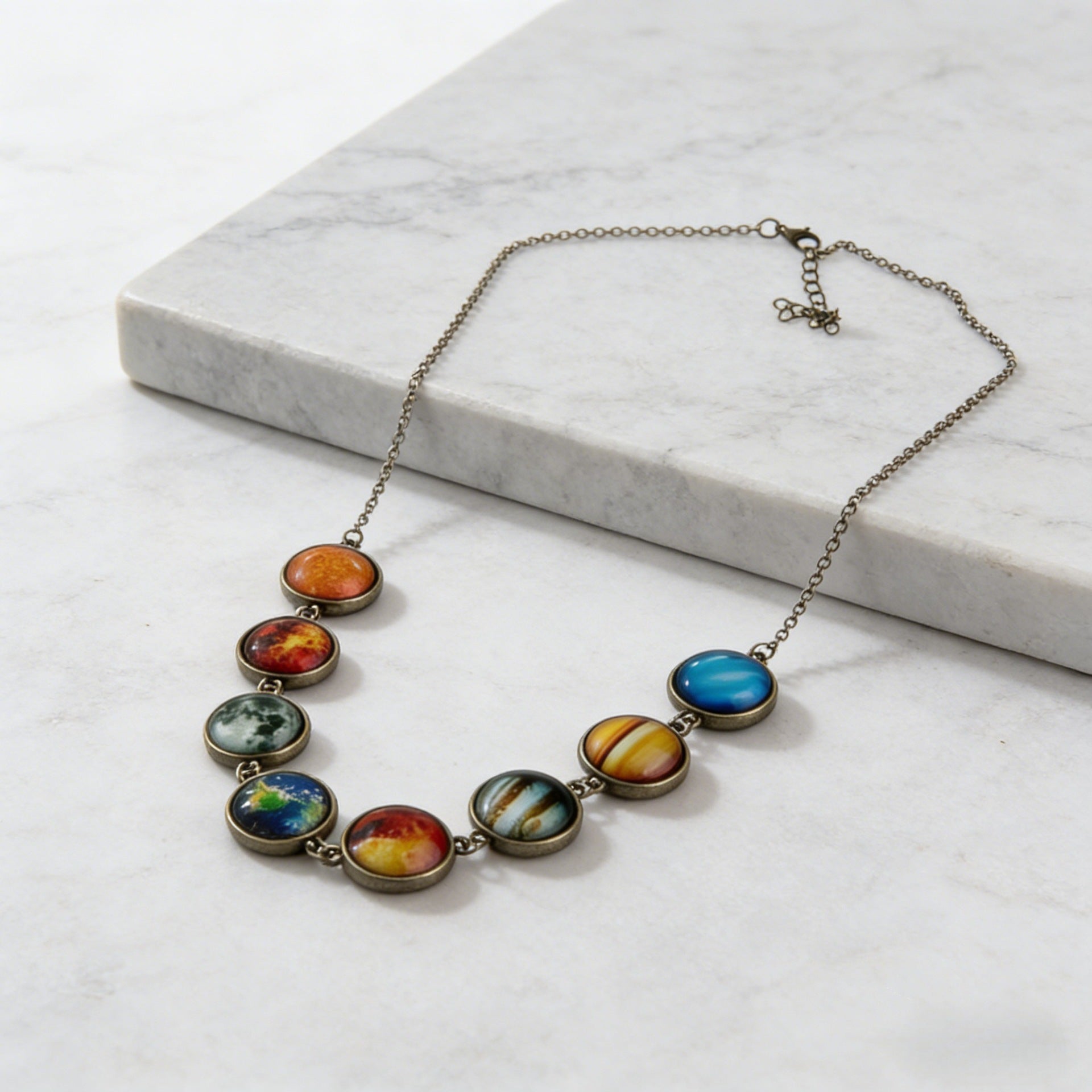 Solar system cabochon necklace on a white marble ledge, eight bezel set domes curving into a low arc
