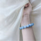 Model wearing the milky blue bead stretch bracelet on the wrist beside soft cream fabric