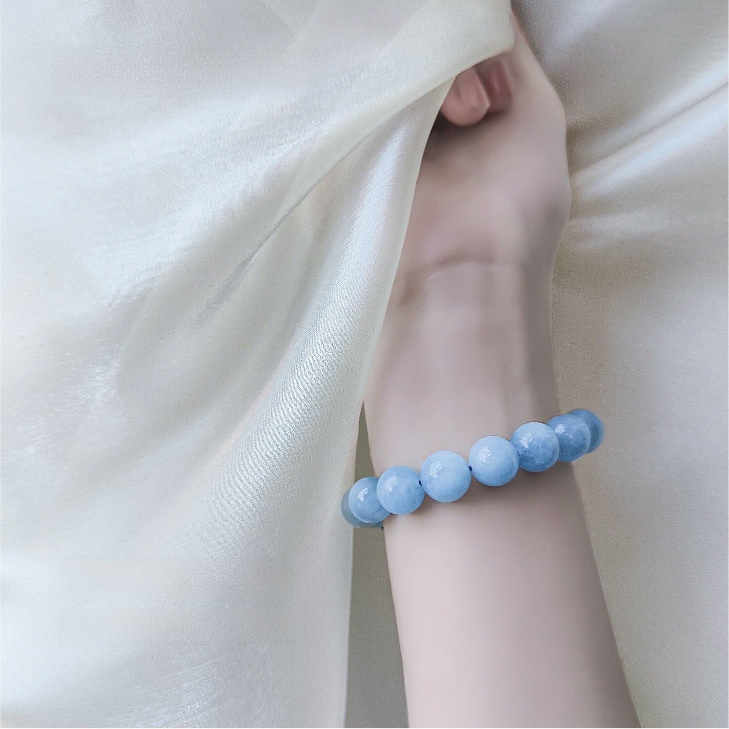 Model wearing the milky blue bead stretch bracelet on the wrist beside soft cream fabric