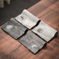 Four tea cloths in light and dark gray with wave roundel and bamboo motifs on a wooden table
