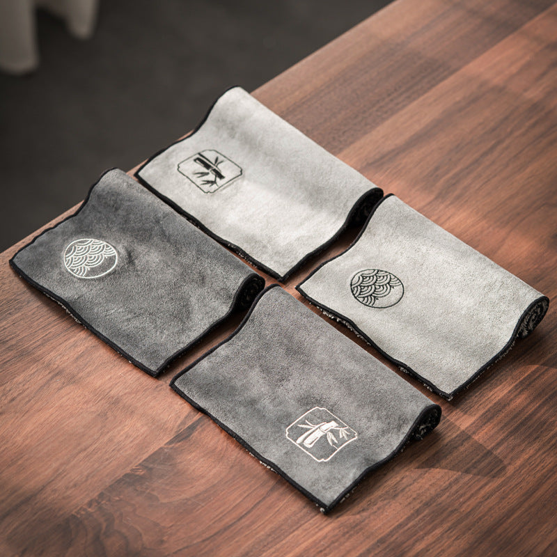 Four tea cloths in light and dark gray with wave roundel and bamboo motifs on a wooden table
