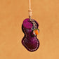 Close view of the purple peanut leather pendant with cream stitching, stamped tag and orange glass fruit bead, purple option