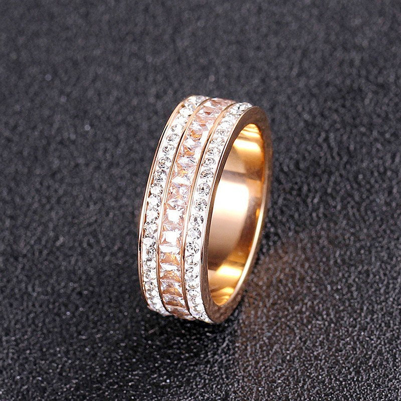 Rose gold tone band ring with three rows of clear stones lying on a dark textured surface