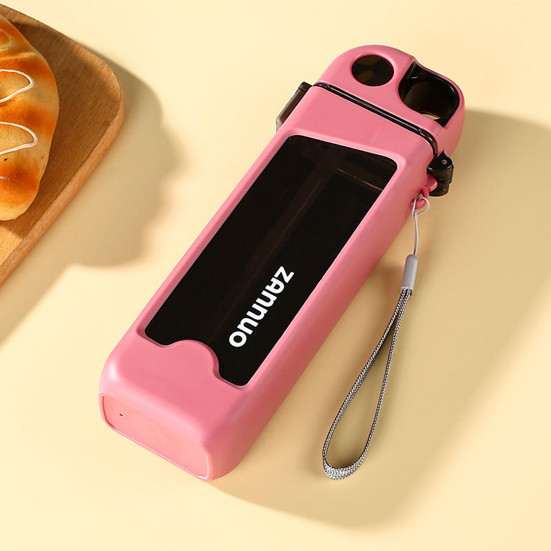 Pink square plastic sports water bottle lying flat with grey woven carrying strap on beige