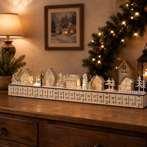White wooden advent calendar village with lit houses and twenty-four numbered drawers on a dresser