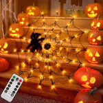 Orange lit spider web net light with a black spider prop draped on steps among glowing pumpkins