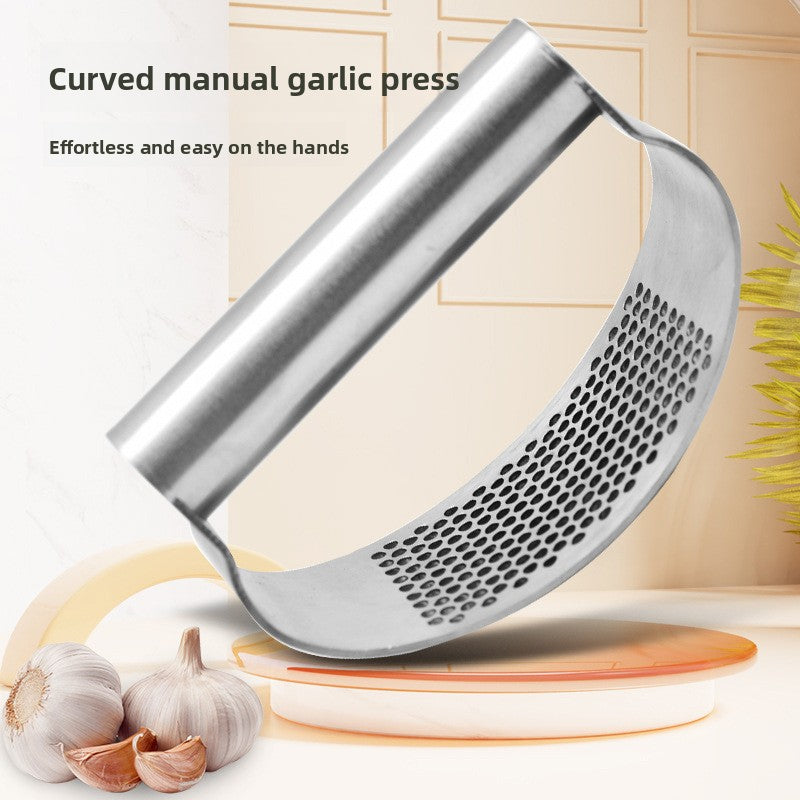 Curved manual stainless steel garlic press standing upright next to whole garlic bulbs