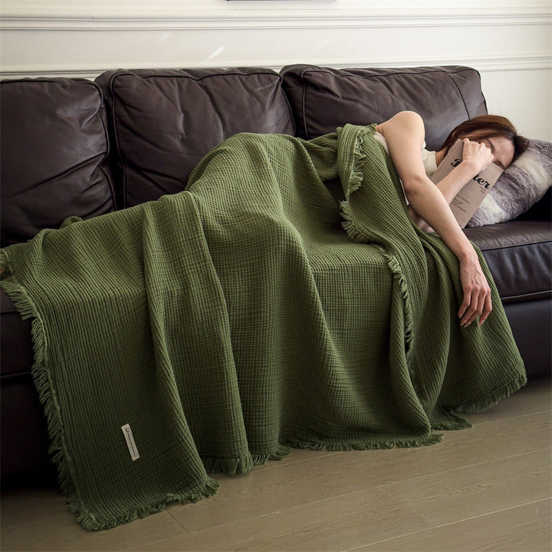 Olive Green cotton gauze throw blanket with tassel fringe, draped over a woman asleep on a dark sofa, view 1 of 4