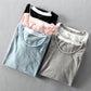 Five folded washed cotton tees in black, pink, light blue, white and light gray, grouped flat lay