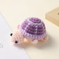 Crocheted purple shell turtle with a pink head, handmade wool charm on a cream surface