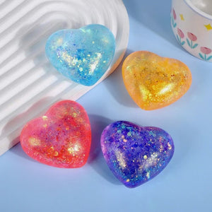 Four aurora glitter heart squeeze toys in blue, orange, red and purple on a pale blue ground
