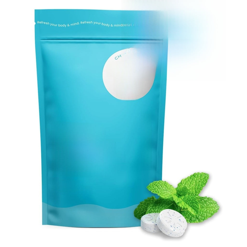 Blue resealable pouch of peppermint caffeine gum with two scored tablets and fresh mint leaves beside it