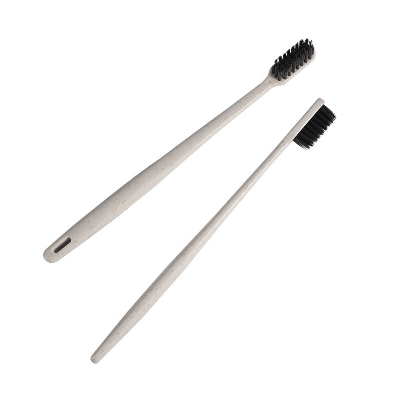 Two beige straw toothbrushes with charcoal bristles laid on a white background