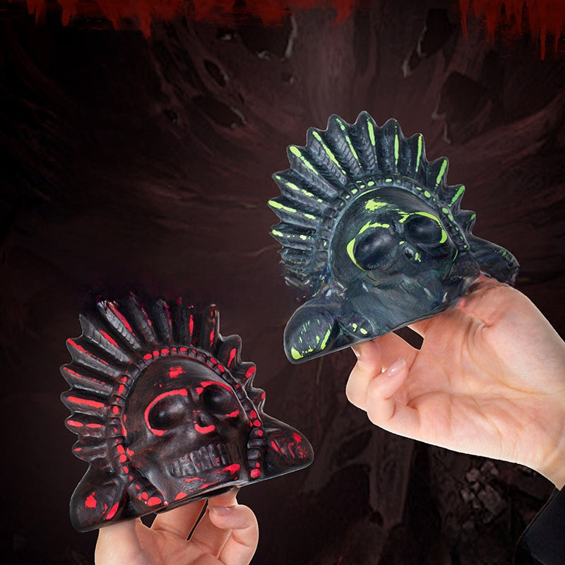 Two hands holding red black and fluorescent green ceramic skull death whistles with feather headdresses