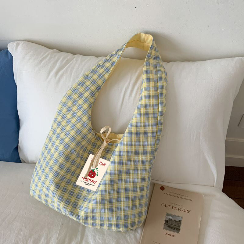 Pink plaid canvas shoulder bag leaning against a bed with a book