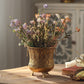 Retro gold iron pot with openwork medallion pattern on three feet filled with flowers beside a book and cup