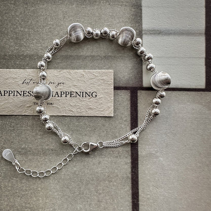 Sterling silver beaded bracelet coiled on a card, brushed beads beside polished rounds