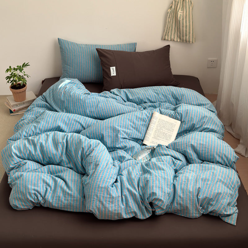 Blue and coral striped cotton quilt cover on a bed with a brown fitted sheet, brown pillowcase, a book and a plant