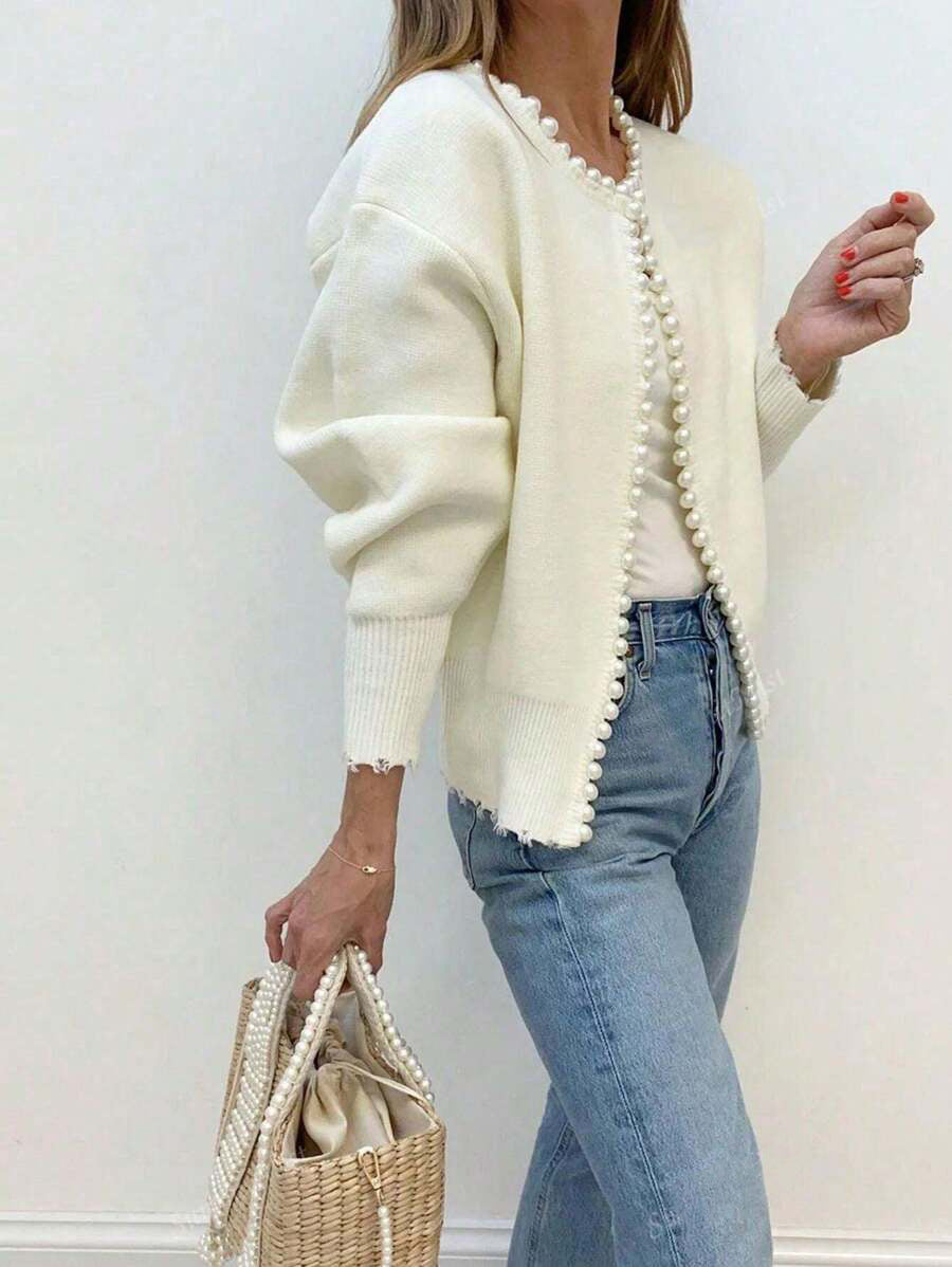 Cream faux pearl trimmed knit cardigan worn open over blue jeans, pearl edged front