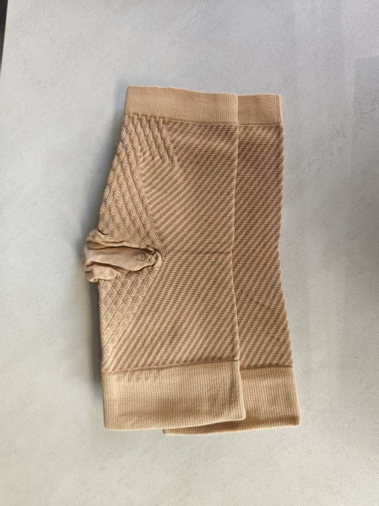 Nude beige knit compression ankle sleeve pair laid flat showing ribbed cuffs and diagonal weave