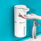 White sensor soap dispenser stuck to a blue wall beside a chrome tap, foam landing on a hand