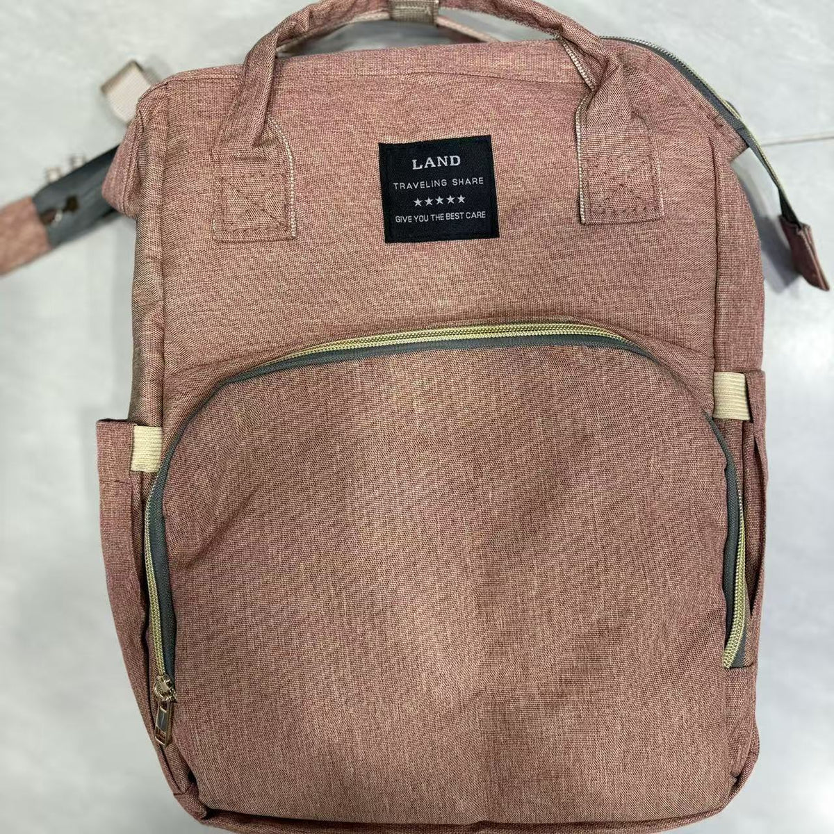 Dusty pink diaper backpack front view on a white surface with two top handles and a front zip pocket
