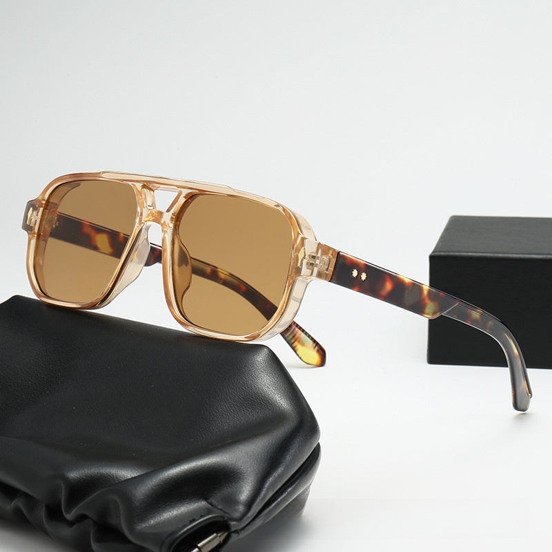 Square double bridge sunglasses with a clear brown frame and brown lenses on a case