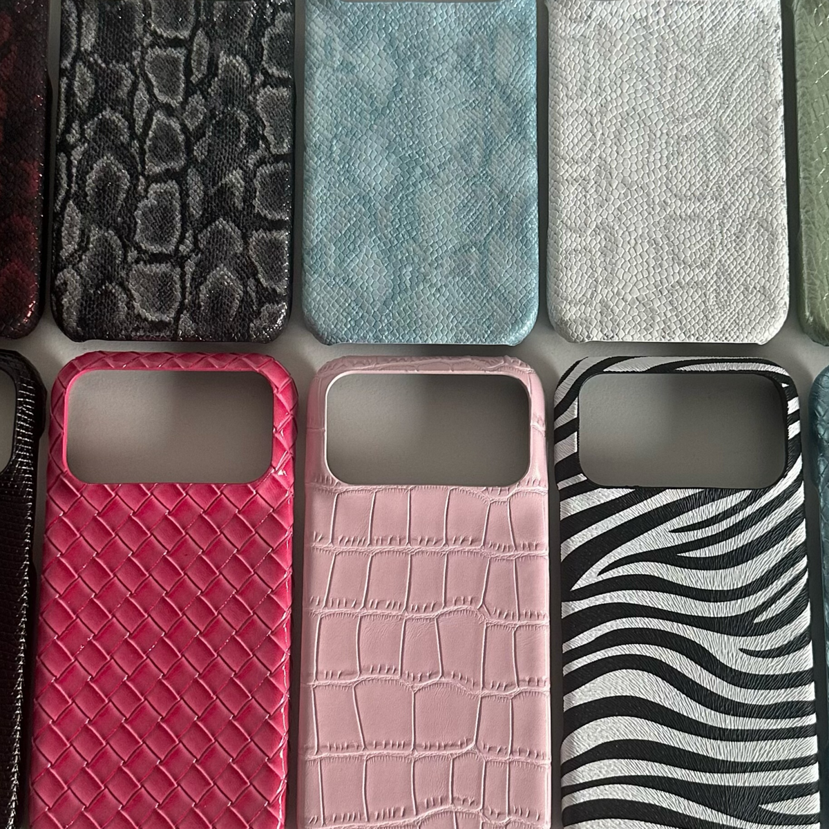 Phone cases in grey snake, blue snake, white snake, red woven, pink crocodile and zebra prints with camera openings