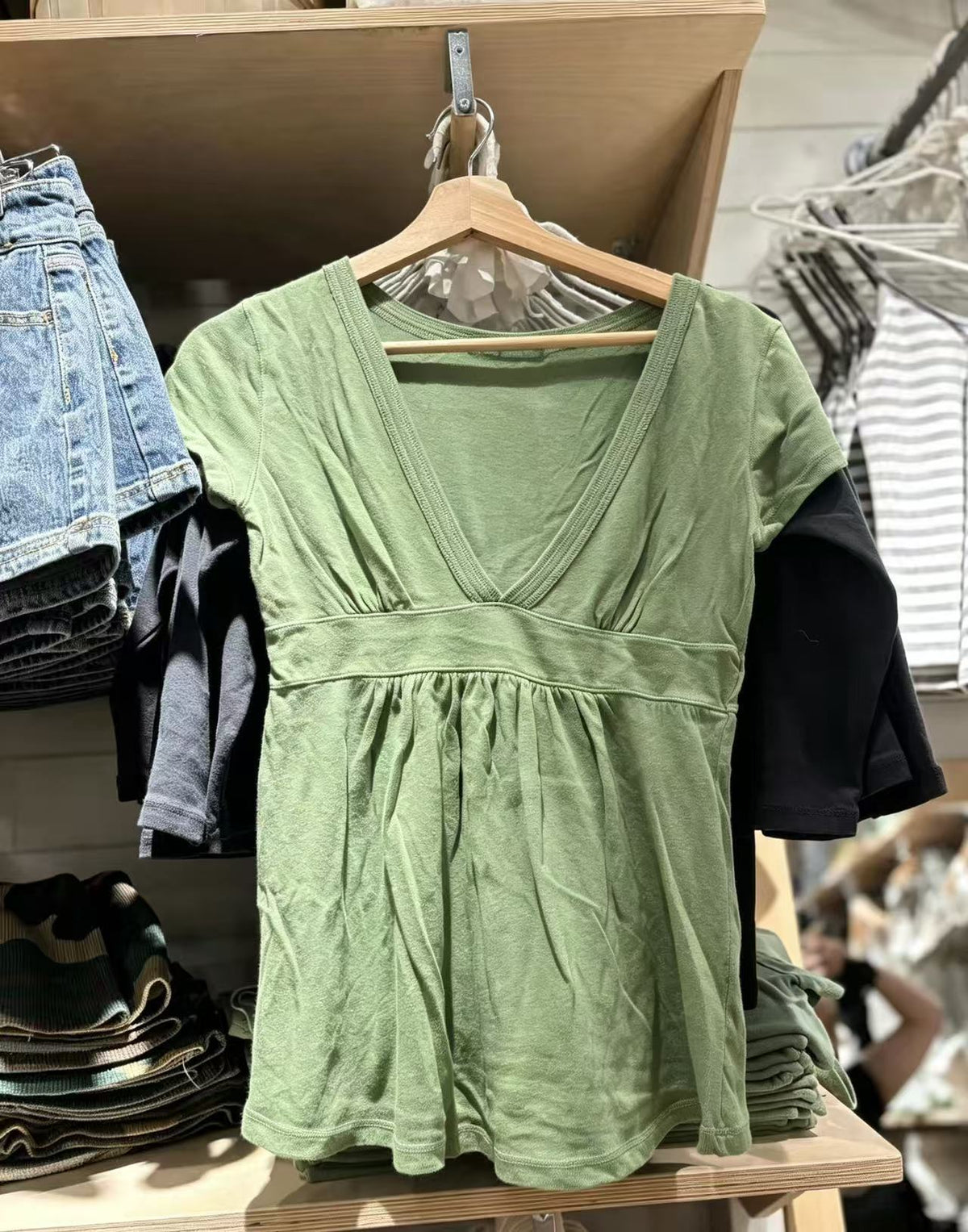 Green short-sleeve deep V-neck top with an empire waist band and gathered hem on a hanger