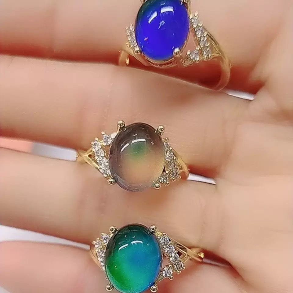 Three gold-tone rings with oval temperature-reactive stones and open adjustable bands seen from the side