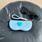 Gray white silicone sunglasses case with an orange raised heart and a braided wrist lanyard