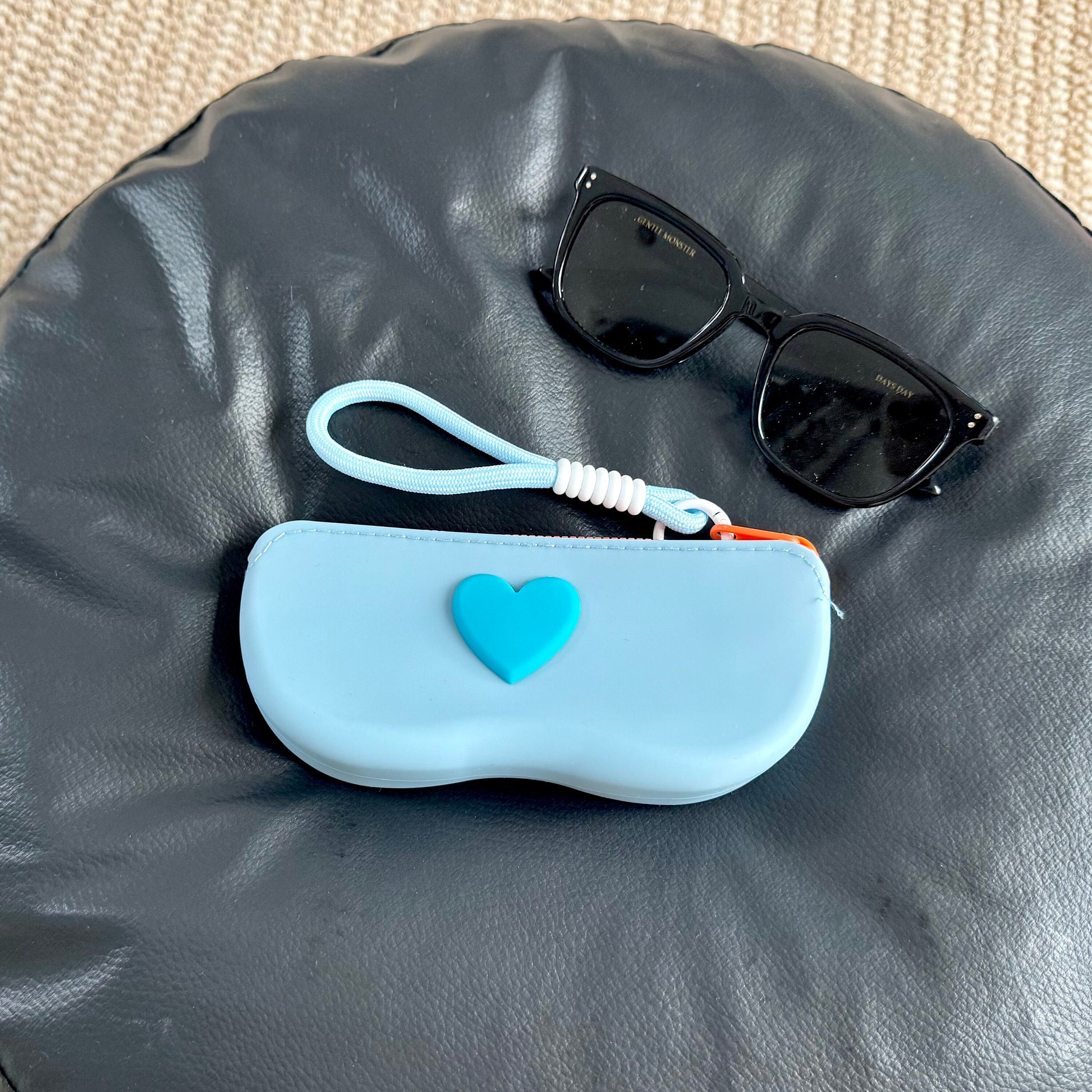 Gray white silicone sunglasses case with an orange raised heart and a braided wrist lanyard