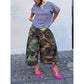 Woman in green camouflage wide-leg pants with a blue and pink striped tee and bright pink heels, full length view