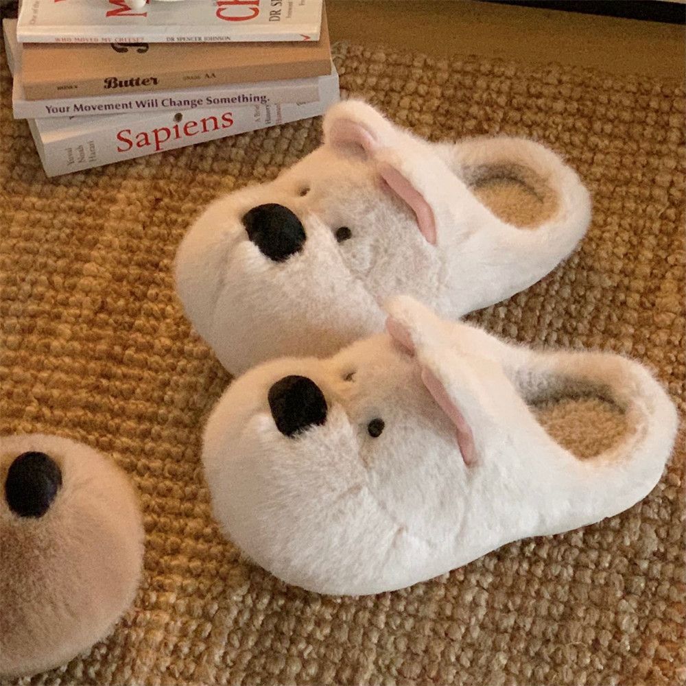 Pair of white puppy face plush slippers with pink ears on a woven jute rug beside a stack of books
