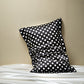 Black silk pillowcase printed with white polka dots, leaning on a beige wall above white silk