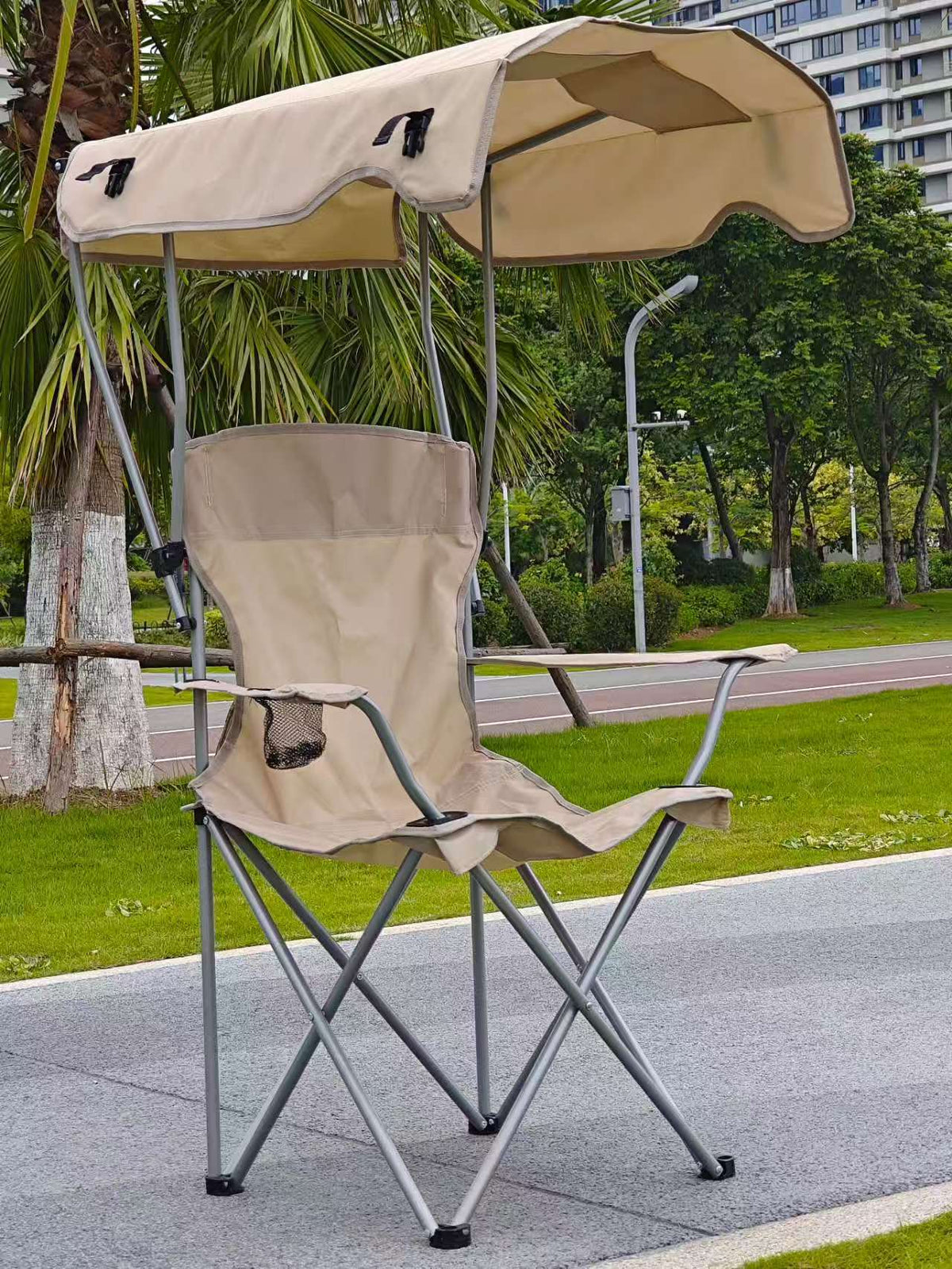 Beige foldable camping chair with a beige canopy and a cup holder on a park path
