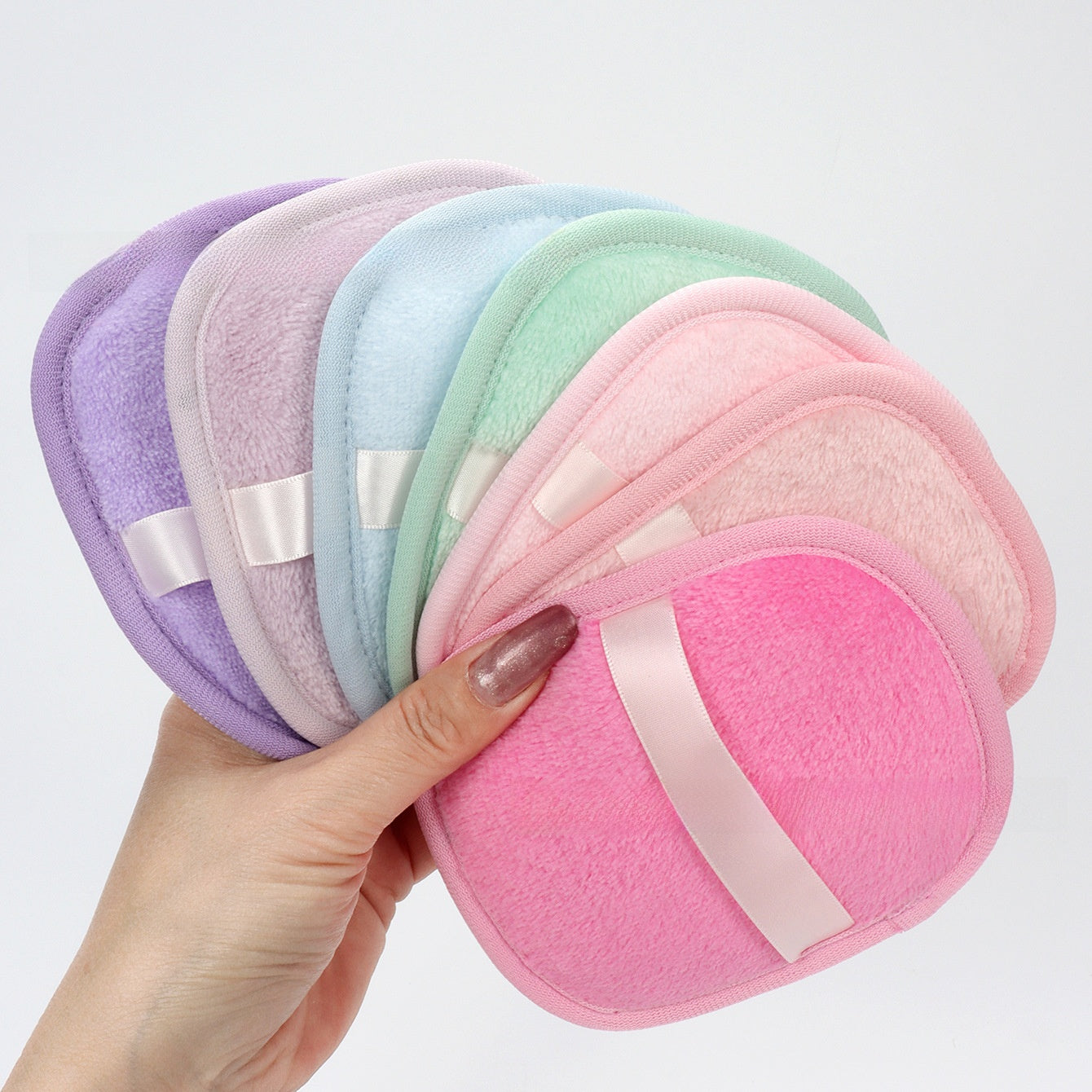 Reusable makeup remover pad with a satin hand strap shown on a plain background