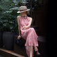 Side view of pink cherry print maxi dress with straw hat outdoors