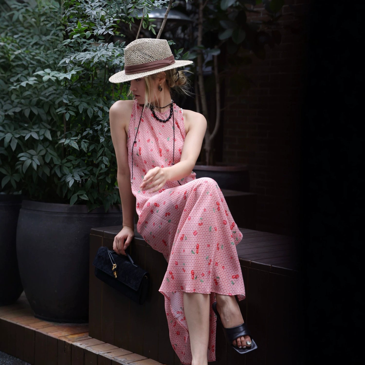 Side view of pink cherry print maxi dress with straw hat outdoors