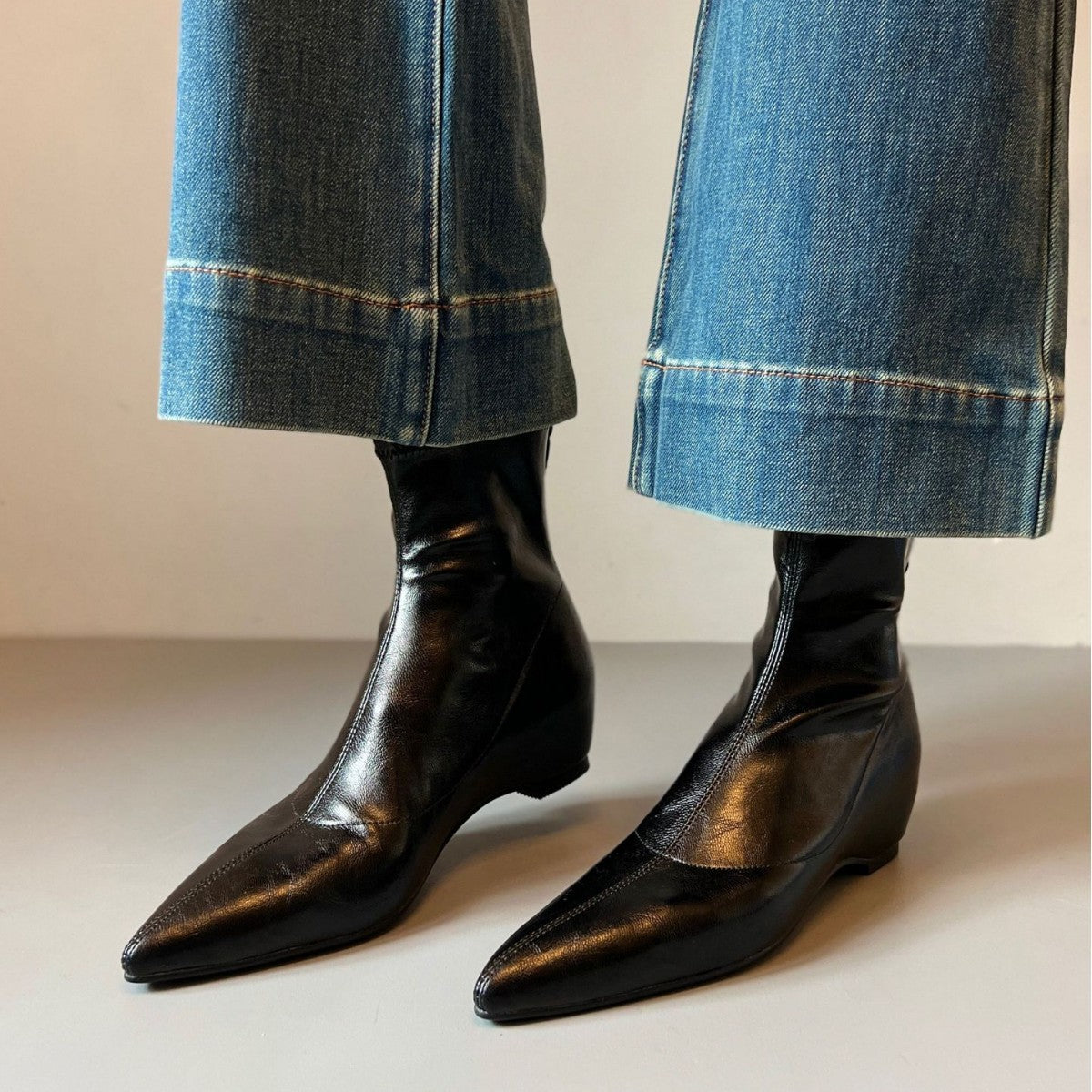 Black pointed toe ankle boots with wedge heels worn under wide-leg blue jeans