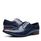Pair of navy blue crocodile embossed pointed toe derby dress shoes with a red brown heel, side view on white